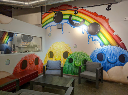 Colorful mural of fluffy creatures under a rainbow, with a cozy seating area in a cafe.